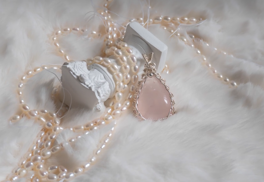 Rose quartz pendant arranged with pearls on a soft white background